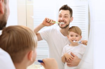 A Father teaches a son how to brush his teeth, promoting healthy dental habits.