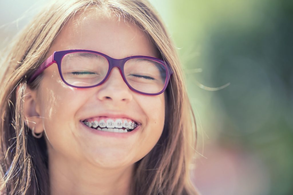 Girl with purple glasses smiling with braces.