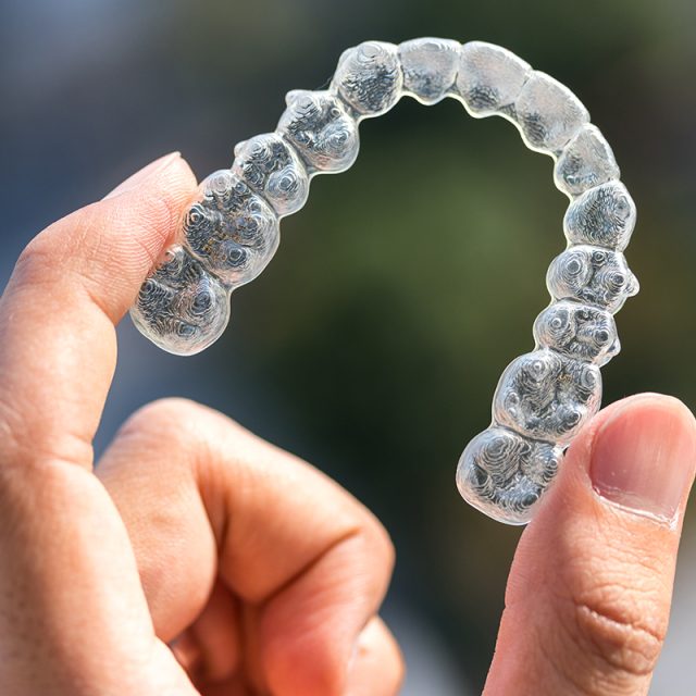 Hand holding up an Invisalign, clear aligner tray.