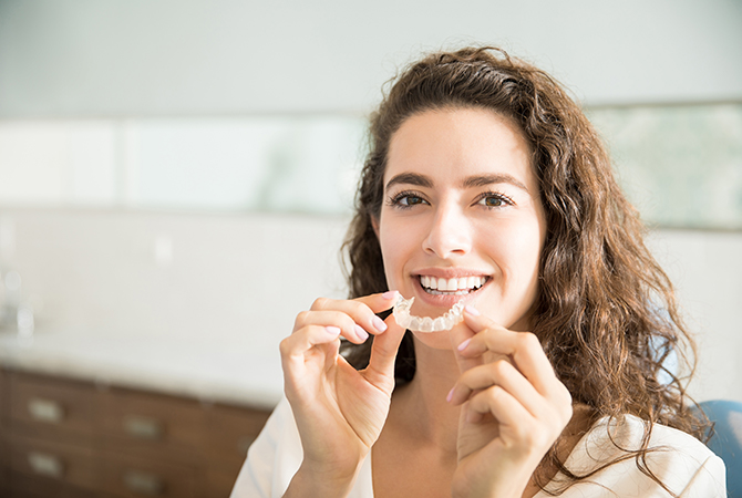 Adult holding orthodontic clear aligners next to her mouth.