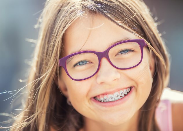Young girl smiling with braces on and purple glasses.